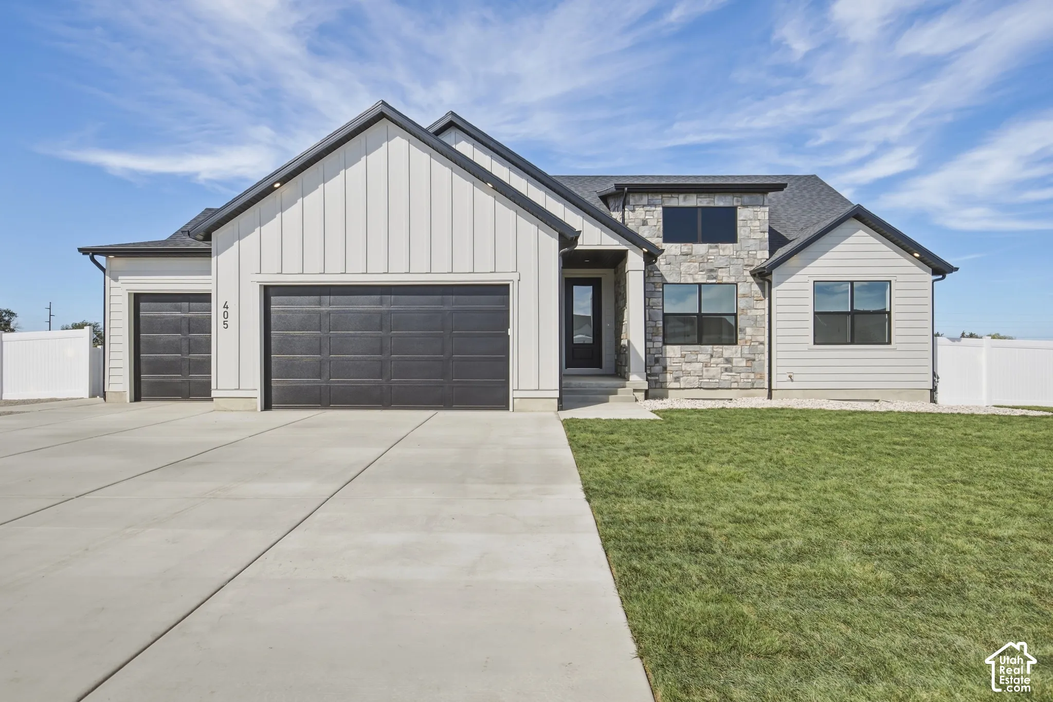 Modern exterior featuring vertical siding, stone accents, black-framed windows, a multi-car garage, and a concrete driveway