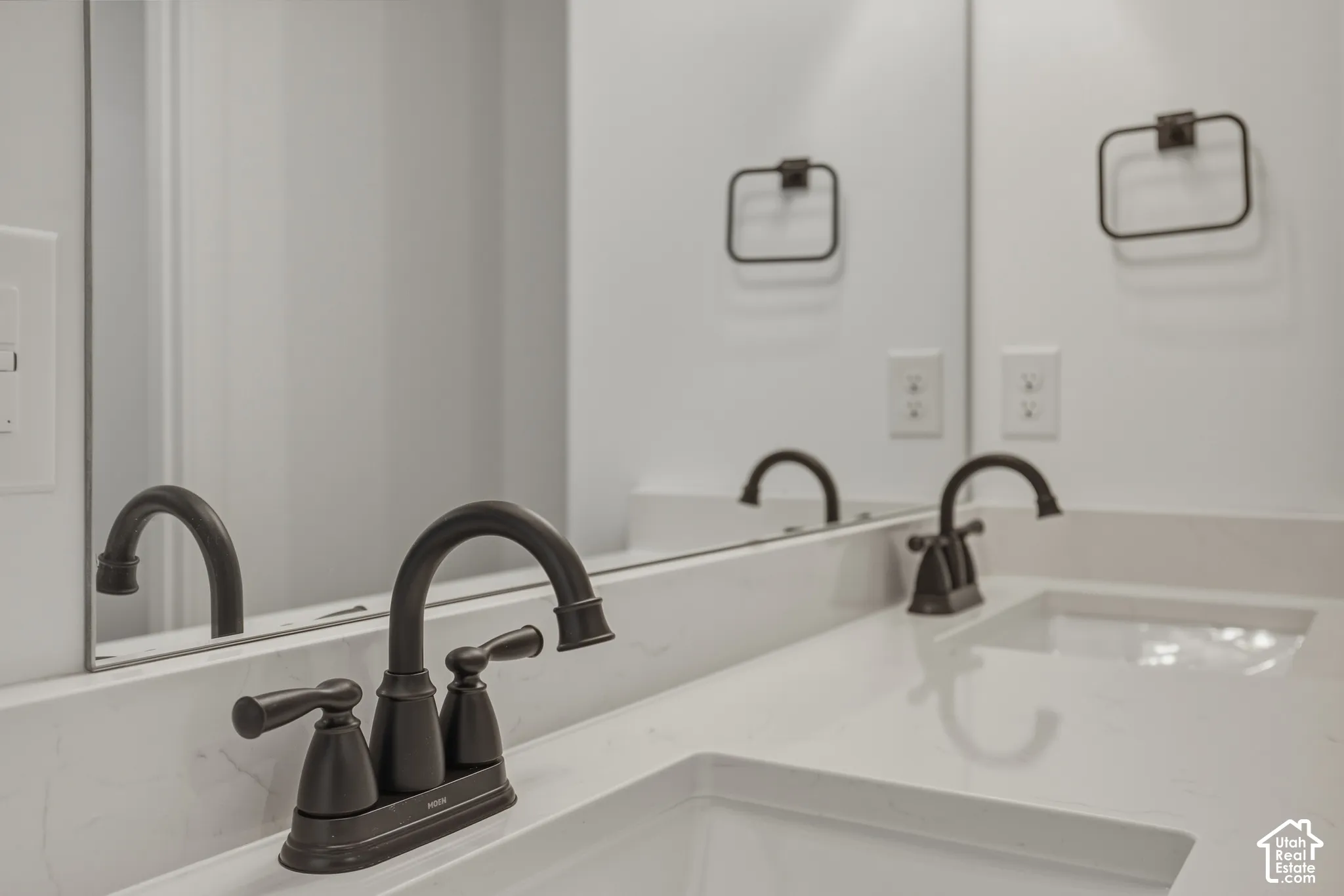 Dual undermount sinks, contemporary dark bronze faucets, and a light-toned countertop with integrated backsplash