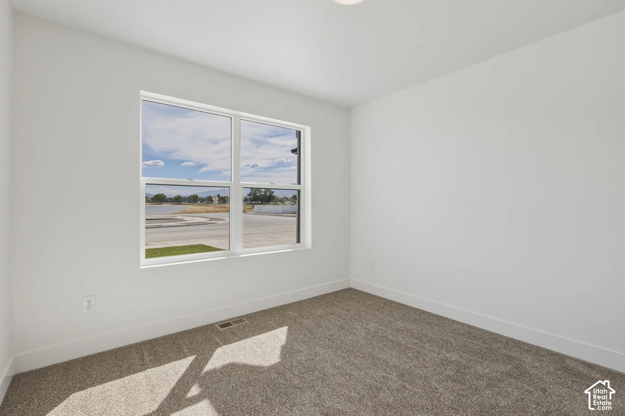 Recessed ceiling lighting, white walls, broad window, and gray carpeting