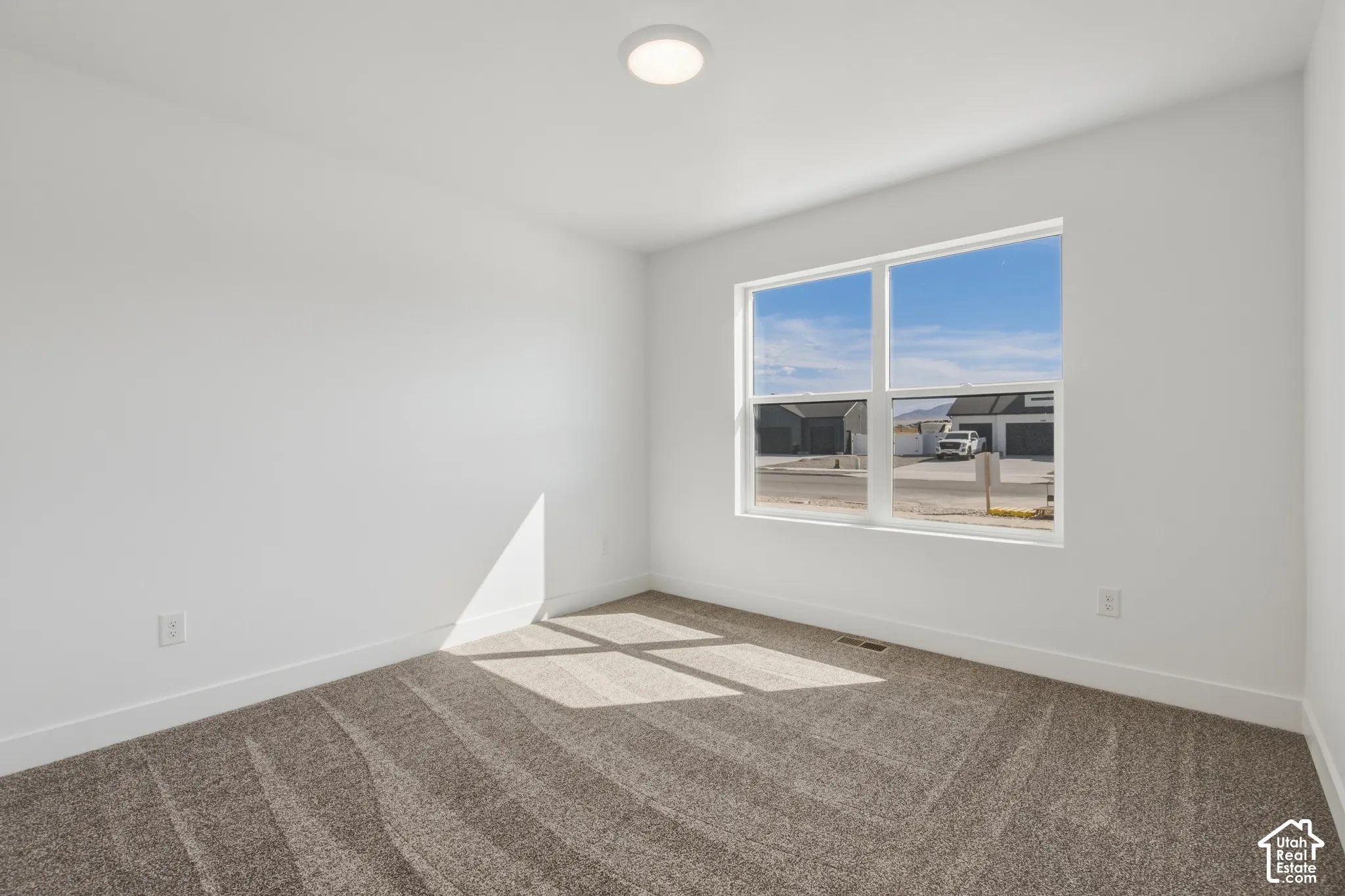 White walls, light gray carpet flooring, large window, flush mount ceiling light