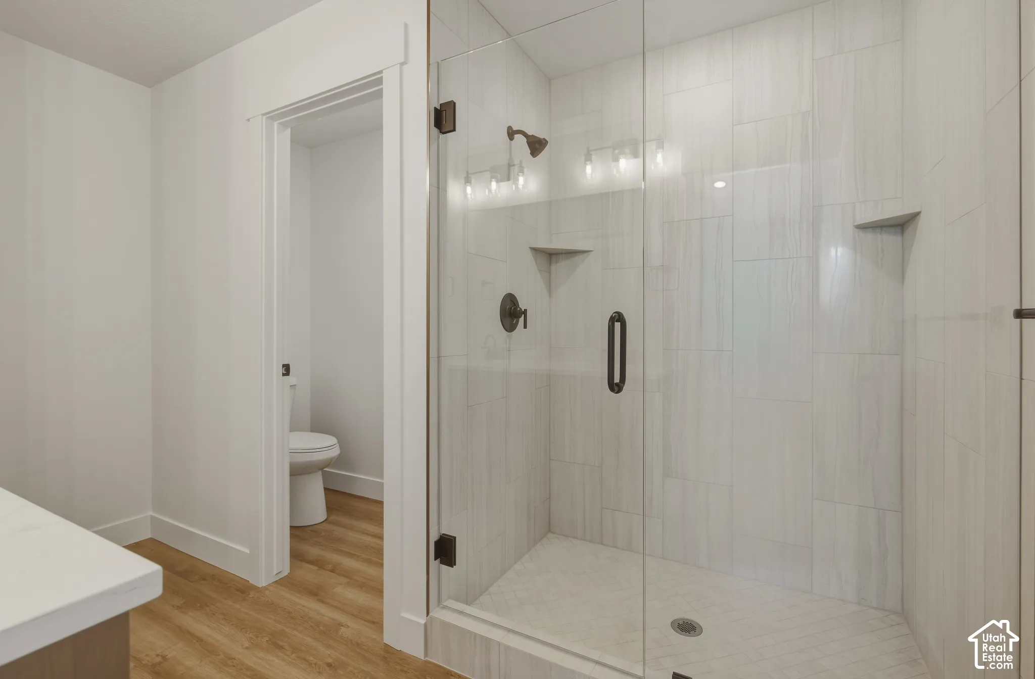 Glass-enclosed shower with vertical-set tile surround, dual built-in shower shelves, and matte black fixtures