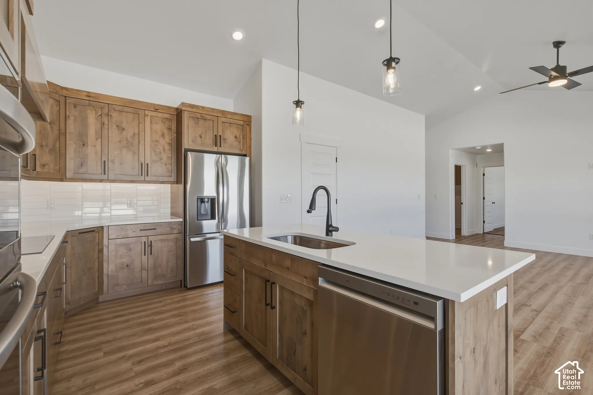 Kitchen featuring wood-finish cabinetry, stainless steel appliances, white subway tile backsplash, and an island with a white countertop and undermount sink