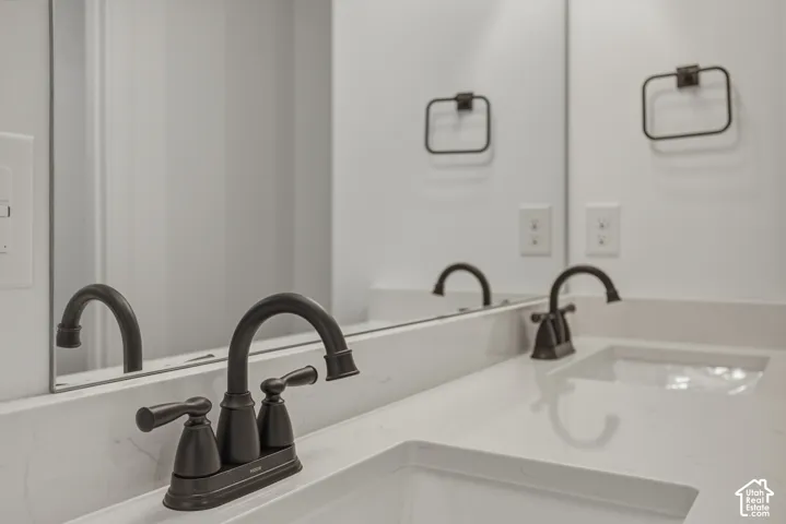 Dual undermount sinks, contemporary dark bronze faucets, and a light-toned countertop with integrated backsplash
