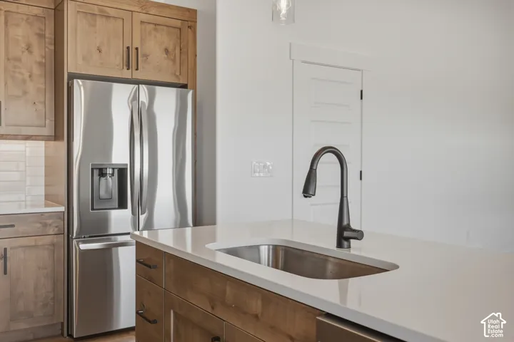Stainless steel French door refrigerator, white solid surface countertop, undermount sink, matte black gooseneck faucet, and wood-finish cabinetry