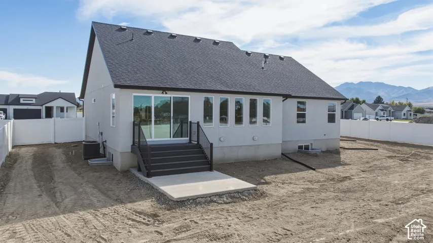 Stucco exterior with a dark shingle roof, featuring a concrete patio and dark-toned stairs with glass panel railing