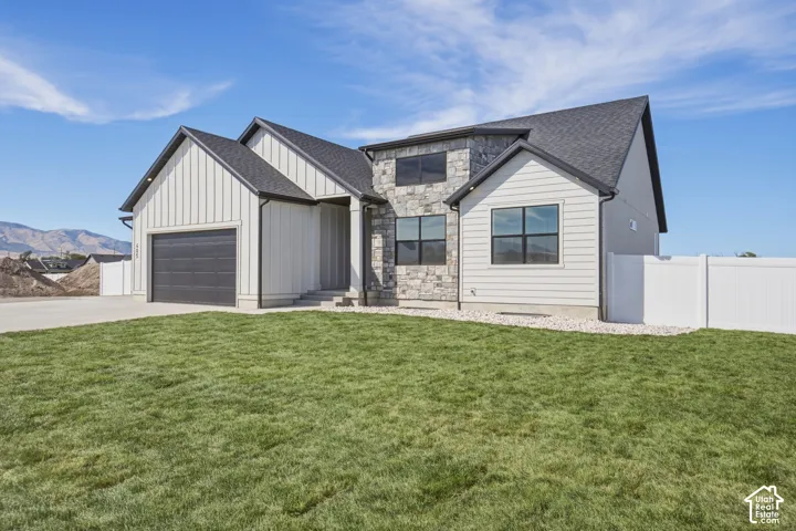 Modern exterior with vertical board and batten siding, stone facade accents, dark-framed windows, an attached garage, and a white privacy fence