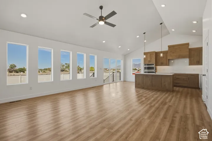 Vaulted ceilings with recessed lighting, wood-finish flooring, multiple large windows, a ceiling fan, and a kitchen featuring wood cabinetry