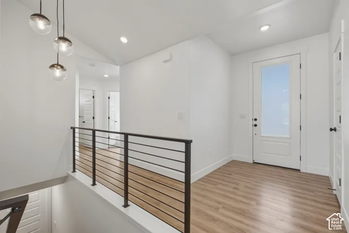 Wood-finish flooring, contemporary glass orb pendant lighting, recessed ceiling lights, white paneled door with frosted glass insert, and black metal railing