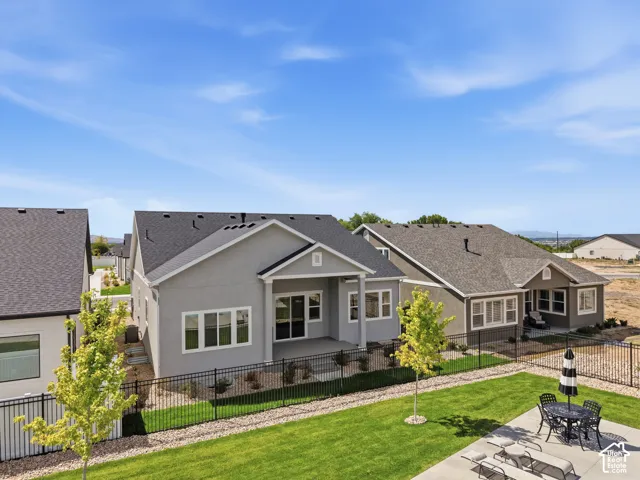 Stucco exterior with a covered patio, multiple windows, and a fenced yard with a manicured lawn