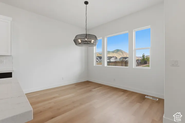 Light wood-finish flooring, multiple windows, contemporary pendant lighting, white walls, and a white quartz countertop