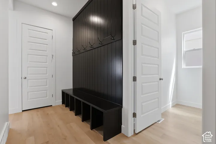 Built-in black storage bench with cubbies, black wainscoting with coat hooks, light wood-finish flooring, white paneled doors, and recessed lighting
