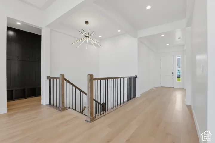 Hardwood flooring, contemporary chandelier, recessed lighting, white walls, and a built-in dark wood accent wall with hooks and bench storage