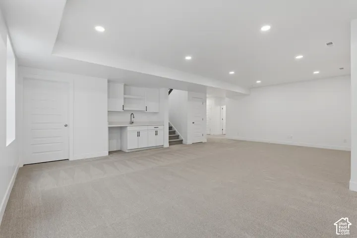 Spacious open area featuring recessed lighting, light-toned carpeting, and a built-in wet bar with white cabinetry and a sink