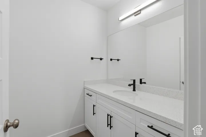 White vanity with shaker-style cabinetry, a speckled countertop, an undermount sink, and a matte black faucet