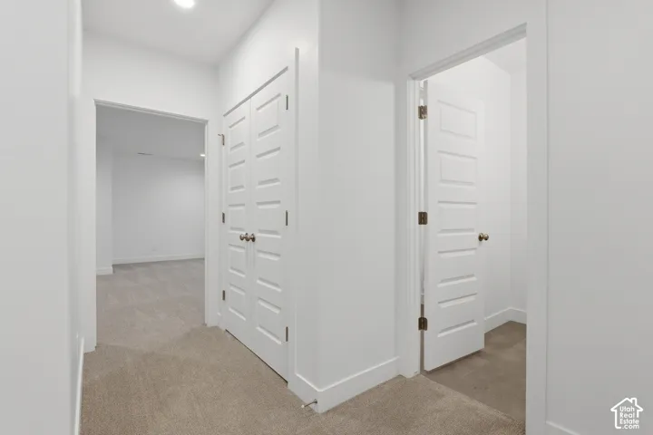 Carpeted hallway featuring a recessed light, two-panel bifold closet doors with round knobs, and a five-panel interior door with a round knob