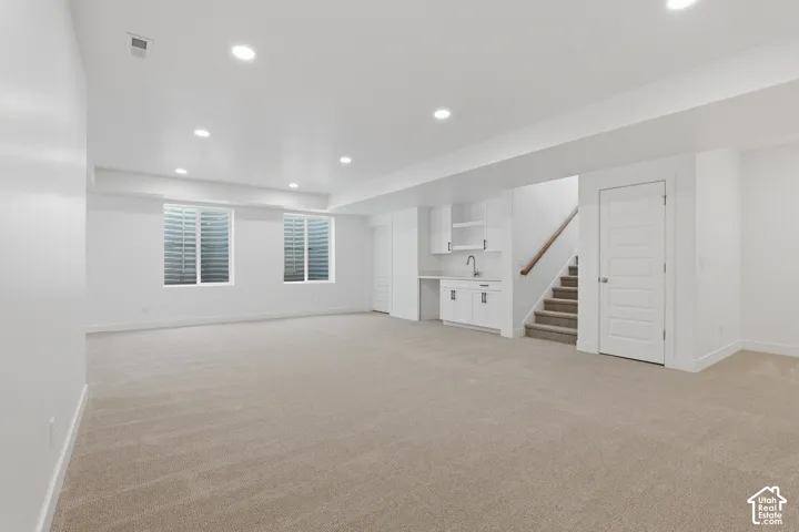 Spacious lower level featuring recessed lighting, two egress windows, a built-in wet bar with cabinetry, and carpeted flooring