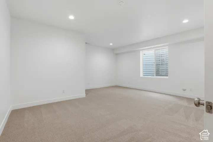 Spacious room with recessed lighting, light-colored carpet, white walls, and a window well