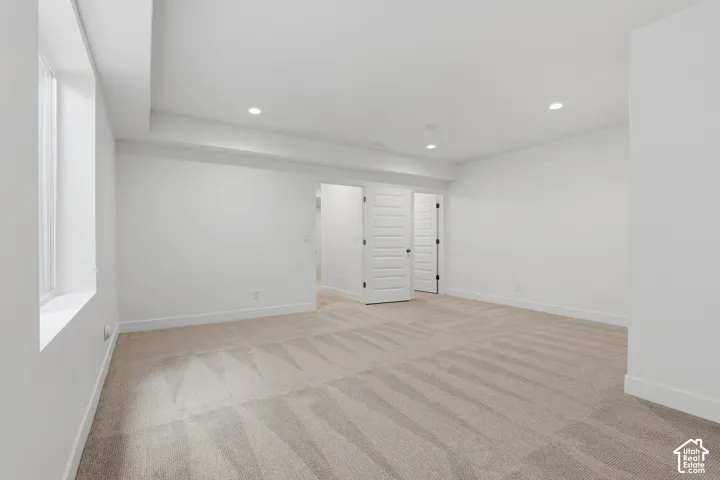 Expansive room with neutral carpeting and a single window, featuring recessed lighting and white paneled doors