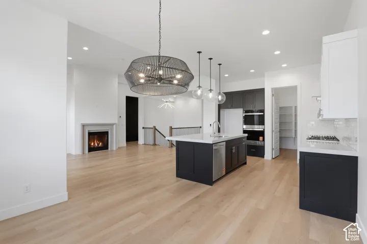 Open-concept living space with light wood-finish flooring, a built-in fireplace, and a kitchen featuring a central island with a sink and pendant lighting