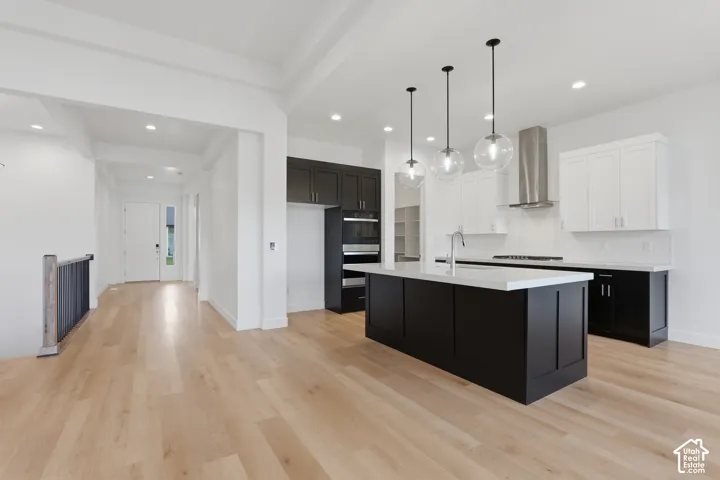 Kitchen featuring a large island with white countertop, pendant lighting, stainless steel range hood, two-tone cabinetry, and wood-finish flooring throughout