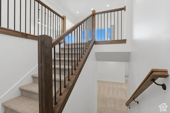 Staircase featuring wood railings with black balusters, carpeted treads, and a recessed ceiling light