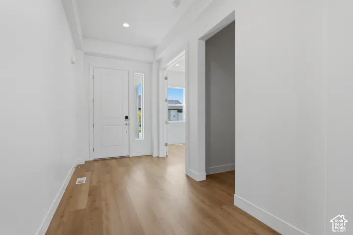 Recessed ceiling lighting, light wood-finish flooring, white walls, white paneled door, and a full-length sidelite window