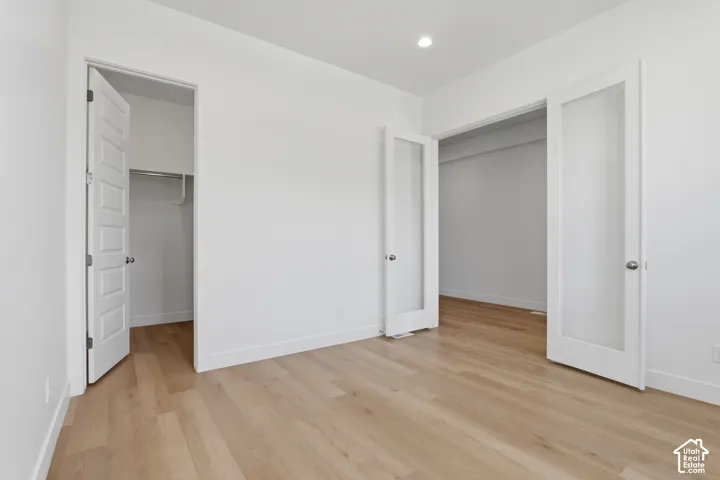 Light wood-finish flooring, recessed lighting, white interior walls, white trim, and white paneled doors