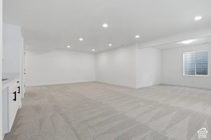 Expansive room with recessed lighting, light-toned patterned carpeting, and white walls