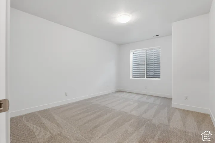 White walls, window well, flush mount ceiling light, and patterned carpet flooring
