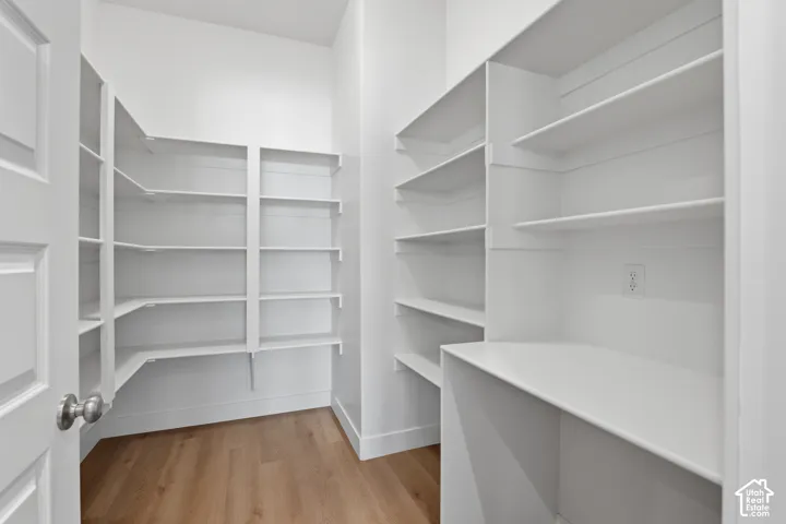 Spacious pantry featuring extensive white shelving, wood-finish flooring, and a built-in countertop with an electrical outlet