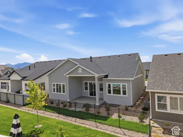 Rear exterior featuring a covered patio, multiple windows, and a landscaped yard with a black metal fence