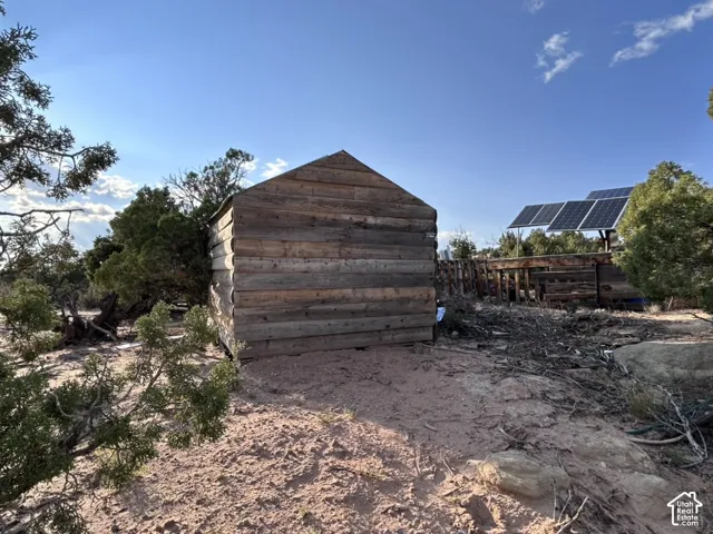 Wood-clad shed with a pitched roof, surrounded by natural landscaping, with visible solar panels