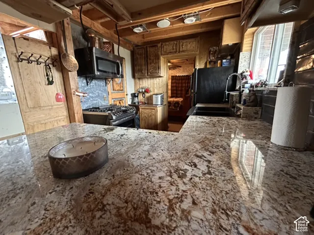 Multi-toned countertop, stainless steel over-range microwave, gas range, wood-finish cabinetry, and exposed ceiling beams