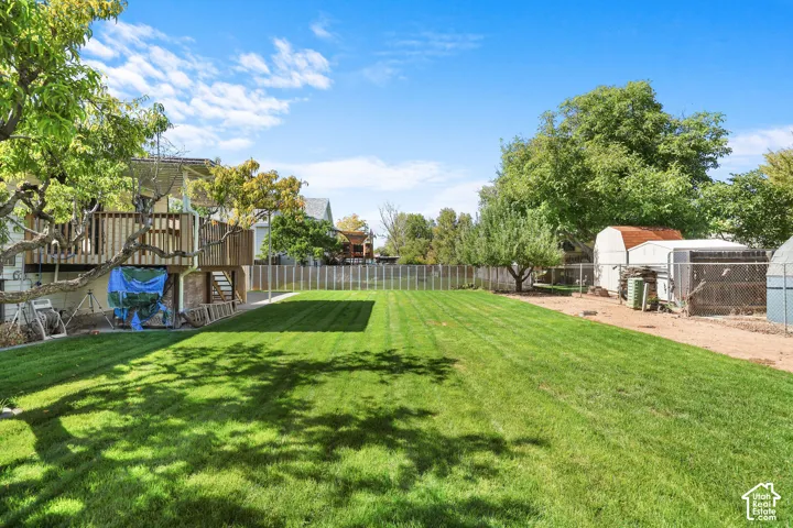 Expansive backyard featuring a manicured lawn, mature trees, and a wooden deck structure