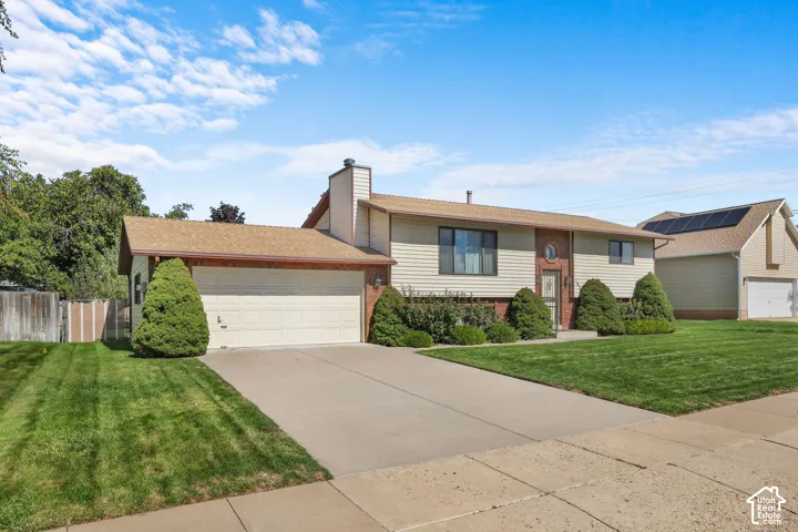 Split-level residence featuring a two-car garage, front yard landscaping, and an asphalt shingle roof