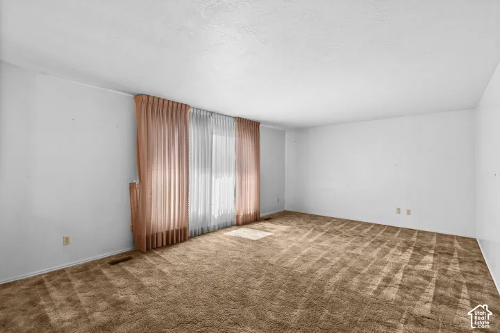 Spacious room with expansive wood-finish flooring, abundant natural light from large windows, and floor-to-ceiling drapery in neutral tones
