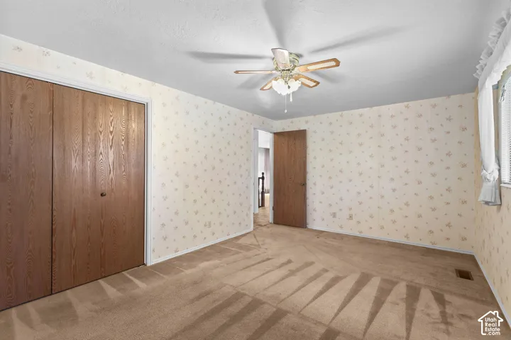 Ceiling fan with light fixture, wood-finish bi-fold closet doors, wall-to-wall carpeting, and window with blinds