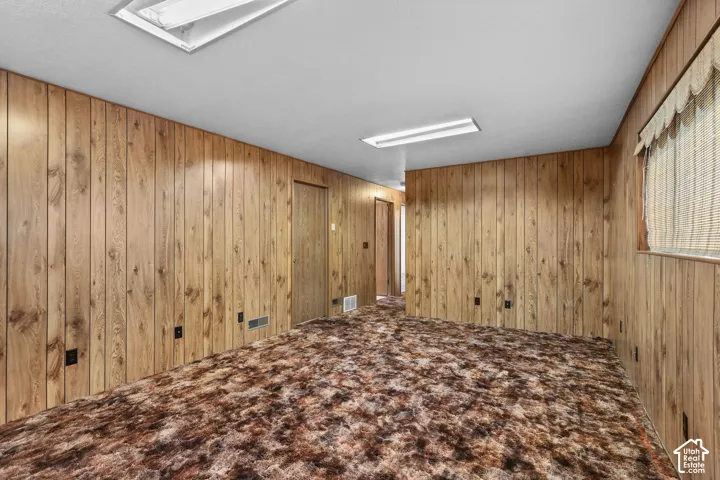 Wood-paneled walls with multiple electrical outlets, brown patterned carpeting, and white ceiling with integrated lighting