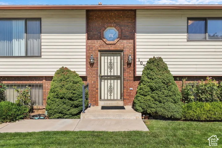 Brick and siding facade with a security screen door, decorative entry sconces, and mature shrubbery