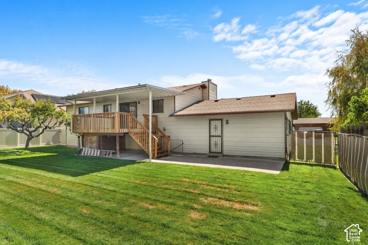 Expansive green lawn, elevated wood deck with railing, covered patio area, vinyl siding exterior, and chain-link fencing