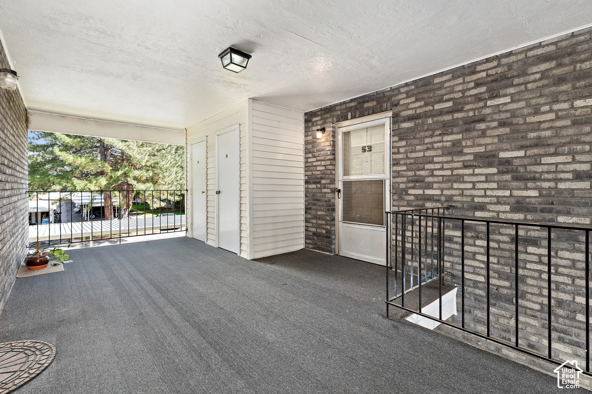 Covered outdoor corridor featuring textured walls, overhead lighting, and a dark railing