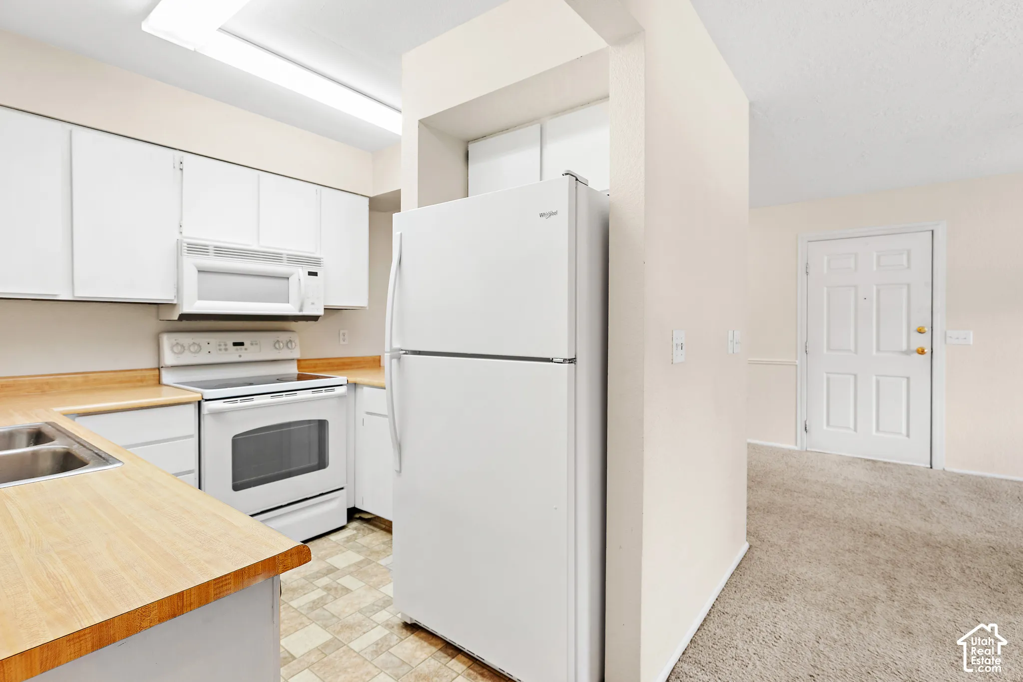 Kitchen featuring wood-finish countertops, white cabinetry, a double basin sink, and white appliances including a refrigerator, range, and microwave