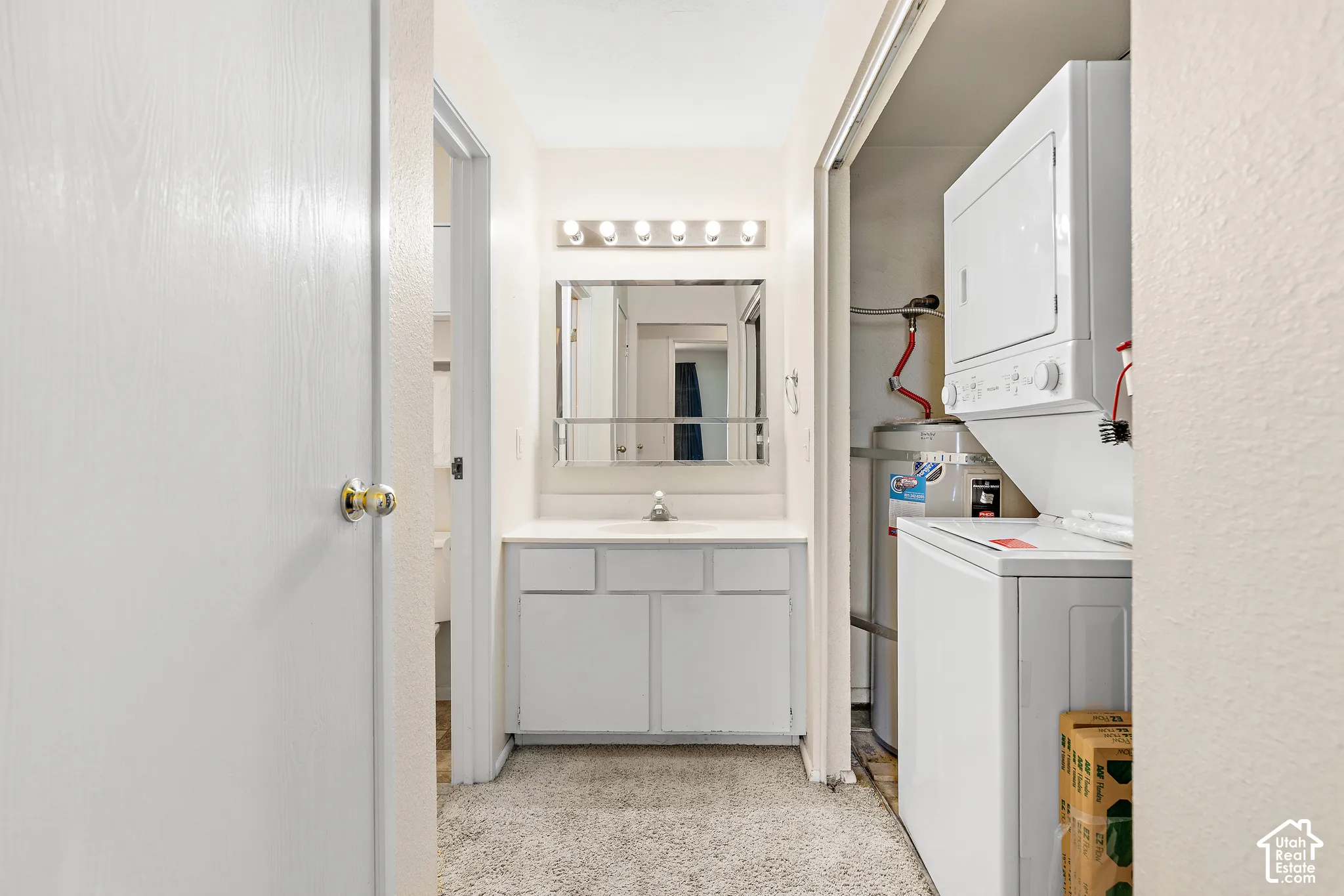 Bathroom vanity with a single sink and wall-mounted light fixture, adjacent to a stacked washer and dryer unit