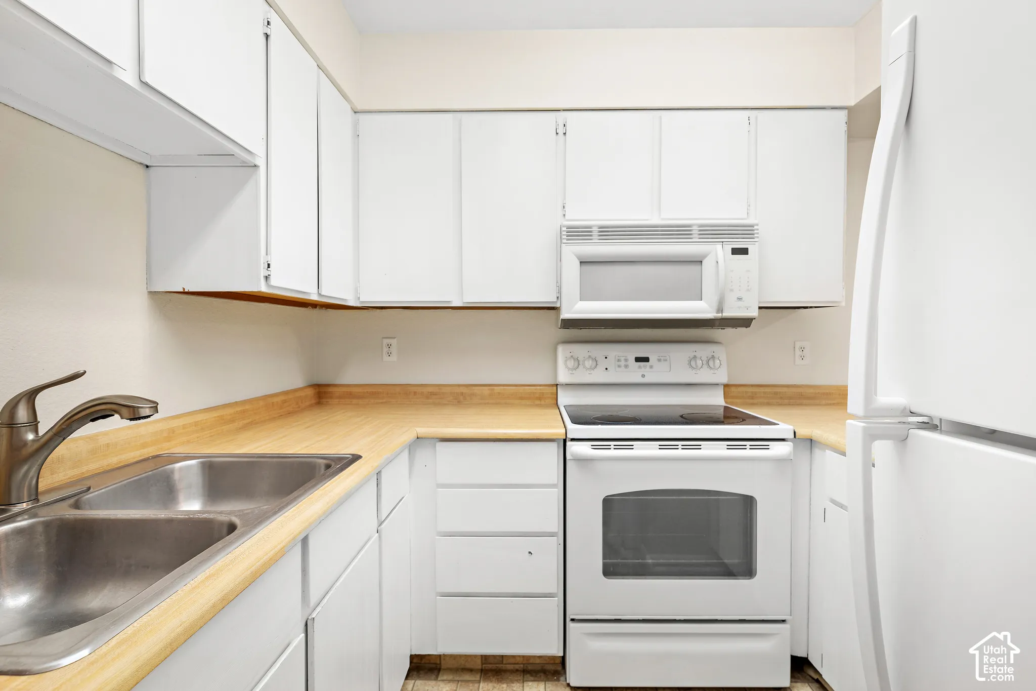 White cabinetry with wood-finish countertops, stainless steel double basin sink, and an electric range with an overhead microwave