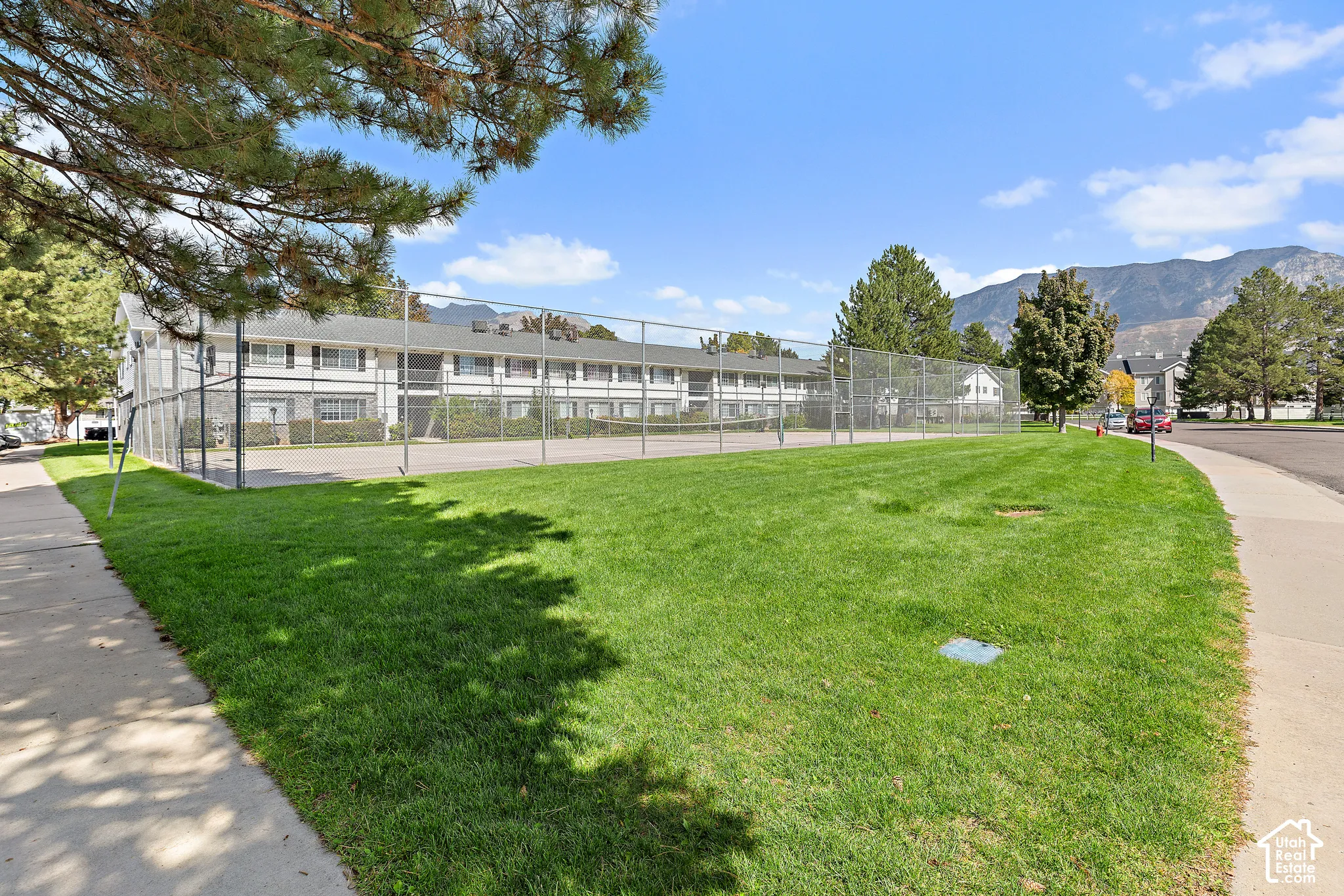 Expansive green space with a chain-link fence, a paved walkway, and a distant mountain backdrop