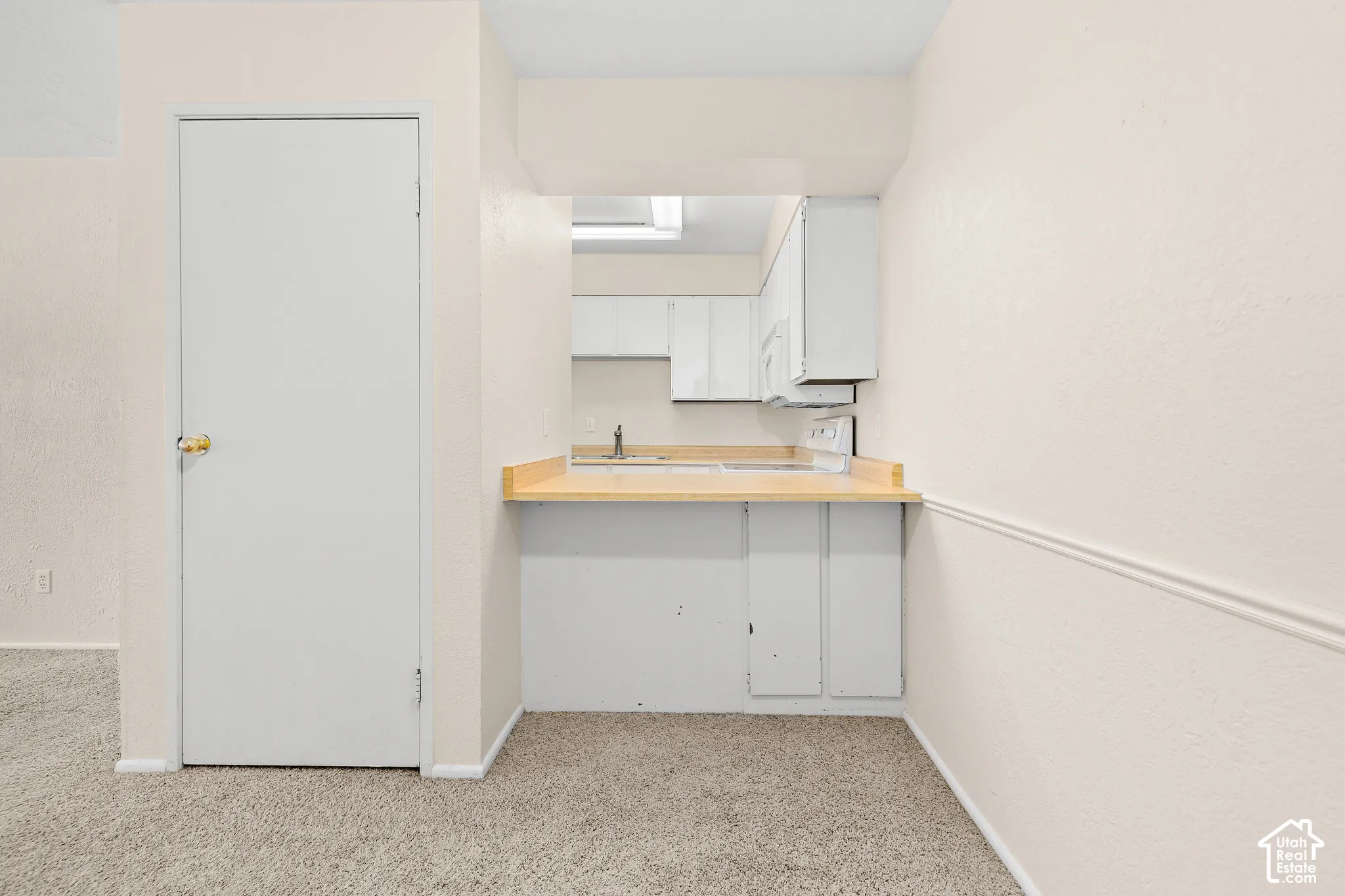Kitchen pass-through with wood-finish countertop, stainless steel sink, and white cabinetry