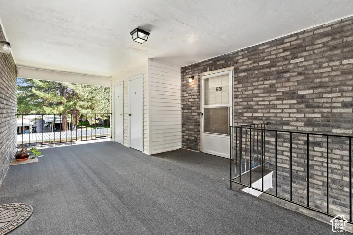 Covered outdoor corridor featuring textured walls, overhead lighting, and a dark railing