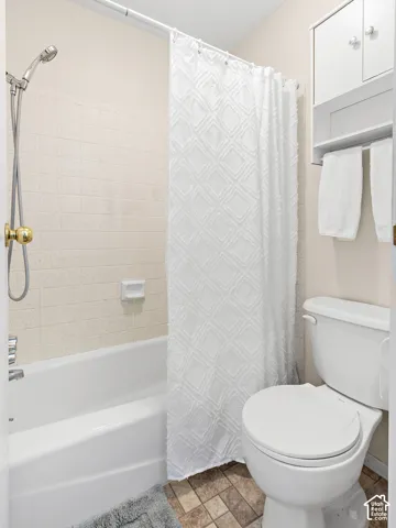 Bathtub with tiled surround and shower fixture, white toilet, and wall-mounted storage cabinet