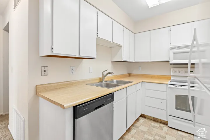 Kitchen featuring white cabinetry, light wood-finish countertops, a double basin stainless steel sink, a stainless steel dishwasher, and a white electric range with an overhead microwave