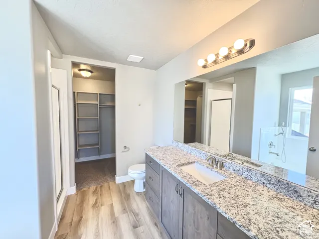 Wood-finish flooring with a glass-enclosed shower, a built-in linen closet, a vanity with stone-finish countertop, and a large mirror with integrated lighting